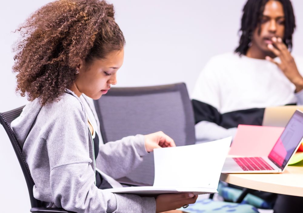 Female student in classroom holding a white notebook and reading through it